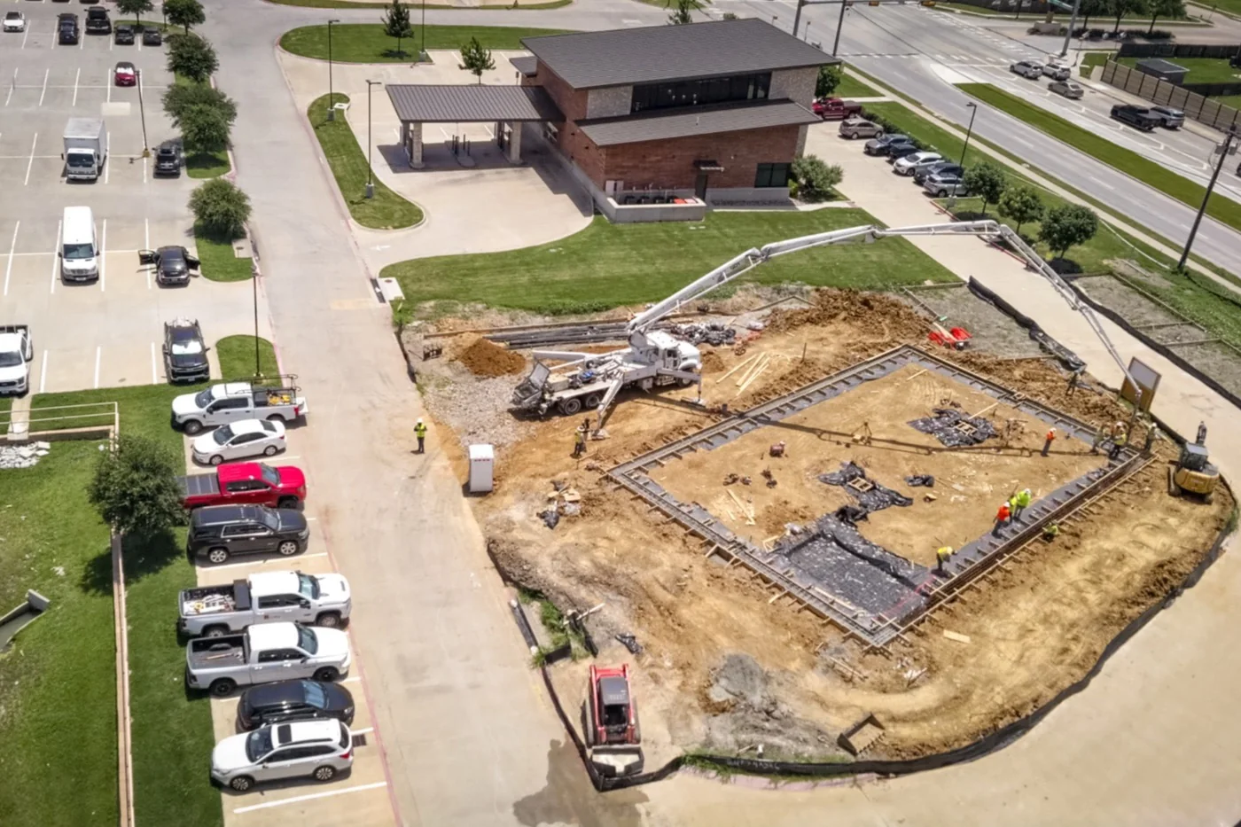 Aerial view of the Anna site in June 2026: the full building footprint laid out in formwork and reinforcement, a concrete pump boom reaching across it, and the parcel in context against the adjacent buildings and road.