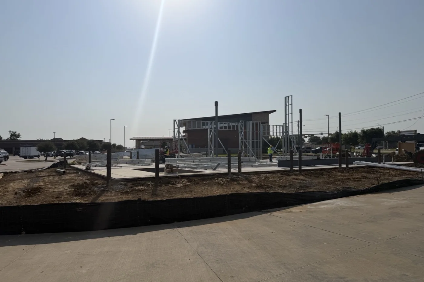 The Anna facility part-framed in August 2026: steel columns standing on the slab with roof members being assembled between them, and the neighbouring building beyond.